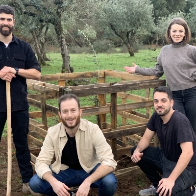 Quatro pessoas junto a uma compostagem de madeira quadrada em área verde com árvores ao fundo