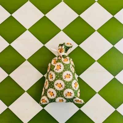 Saco de tecido verde estampado com flores brancas e amarelas sobre piso de azulejos brancos e verdes