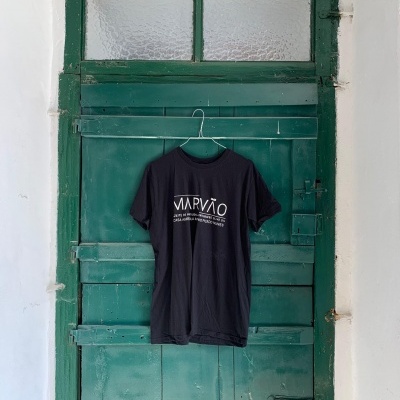 T-shirt preta com texto branco pendurada numa porta verde