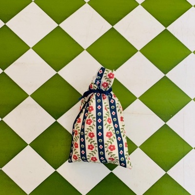 Saco de tecido com padrão floral e riscas azuis sobre chão xadrez verde e branco