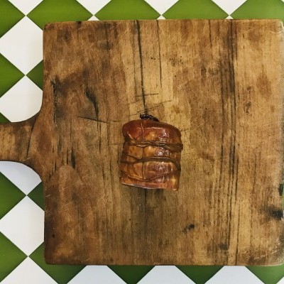 Tábua de madeira rústica com chouriço defumado no centro, sobre azulejos brancos e verdes.