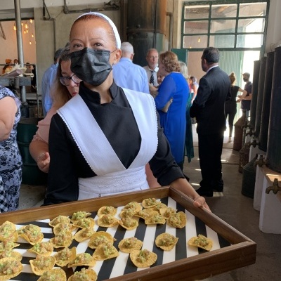 Pessoa trajando vestido preto e avental branco segurando tabuleiro com torradas e patê verde