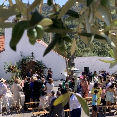 Evento ao ar livre junto a capela branca com ramos de oliveira em primeiro plano