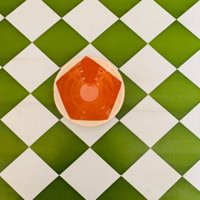 Copo de plástico com líquido laranja sobre pavimento em losangos verdes e brancos