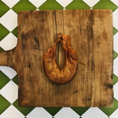 Chouriço em forma de ferradura numa tábua de madeira em tabuleiro com padrão verde e branco