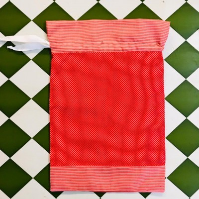 Saco de tecido vermelho com pontos brancos e riscas, fundo xadrez branco e verde