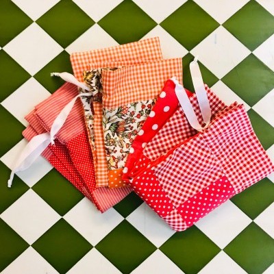 Sacos de tecido coloridos em várias estampas com fitas brancas, sobre azulejos verdes e brancos