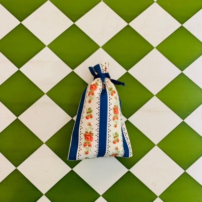 Saquinho decorativo de tecido com padrão floral e faixas azuis e brancas sobre azulejos verdes e brancos em padrão xadrez