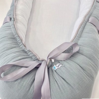 Ninho de bebé cinza e branco com fitas lilás e etiqueta 'Catita Kids'