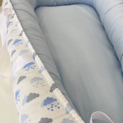 Ninho para bebé azul claro com borda estampada de nuvens cinzentas e azuis