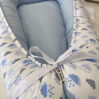 Ninho para bebé azul claro com padrão de nuvens e fita branca.