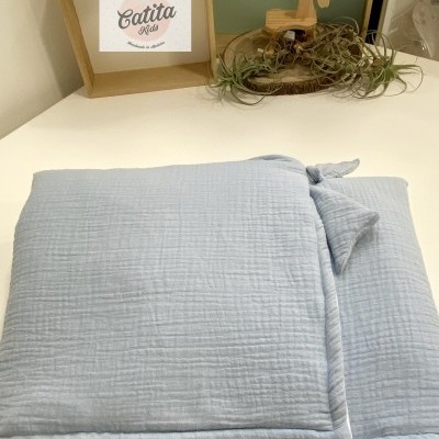 Manta azul claro dobrada com etiqueta Catita numa mesa branca, quadro Catita Kids e decoração com cavalo de madeira ao fundo