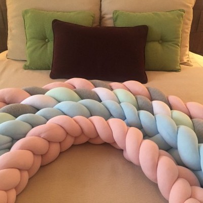 Protetores de cama trançados em tons pastéis sobre cama com almofadas verdes e marrom