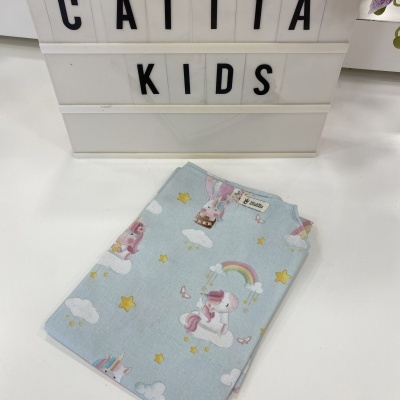 Peça de roupa infantil azul claro com padrão de unicórnios e estrelas dobrada em mesa branca com placa CATITA KIDS ao fundo