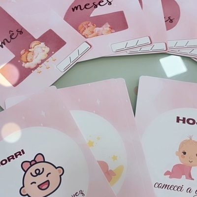 Cartões rosa para bebés com ilustrações e textos em português, dispostos sobre uma mesa clara.