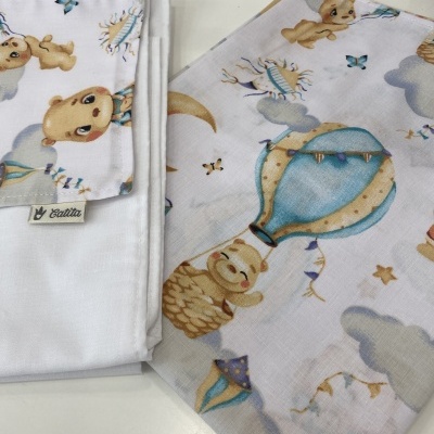 Tecido infantil com balões de ar quente, ursos e nuvens ao lado de pano branco com etiqueta Calitta