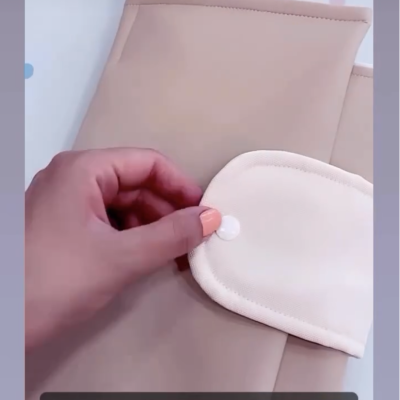 Bolsa multiusos bege com muda fraldas creme, textura de pele, fecho em velcro, sobre superfície branca com pontos azuis.