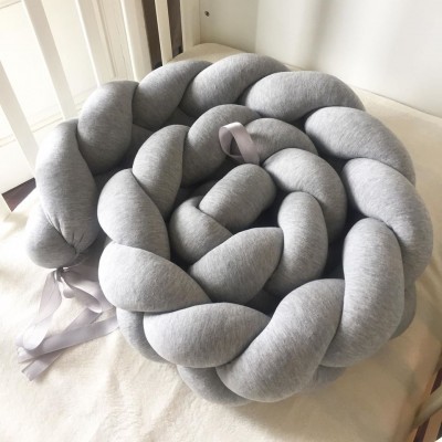 Almofada trançada cinzenta claro sobre superfície clara e madeira