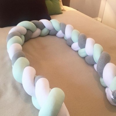 Almofada trançada decorativa em tecido colorido sobre cama com lençol bege