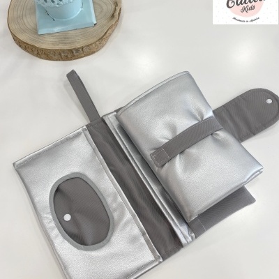 Bolsa ou estojo prateado aberto com compartimento transparente oval e interior cinza, planta em vaso azul ao lado