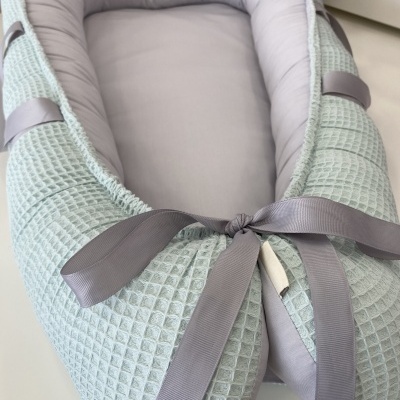 Ninho para bebé verde-água com interior cinza e fitas cinzentas.