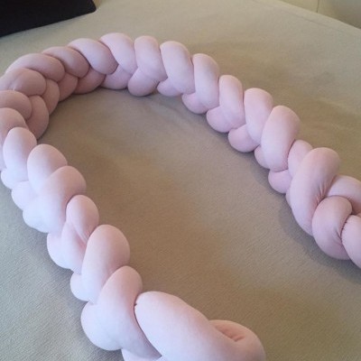 Pala protetora entrelaçada rosa claro sobre cama bege clara