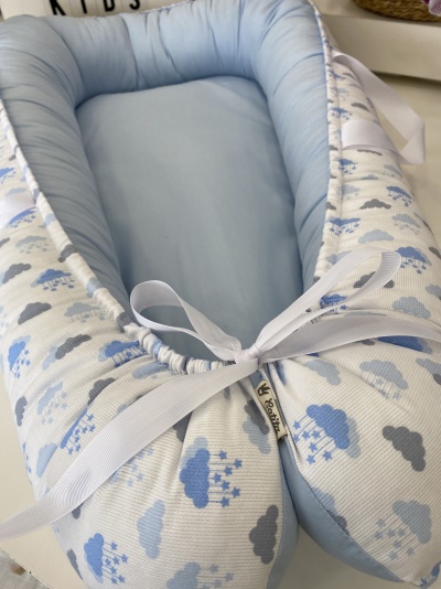 Ninho para bebé azul claro com padrão de nuvens e fita branca.