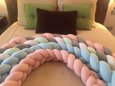 Protetores de cama trançados em tons pastéis sobre cama com almofadas verdes e marrom