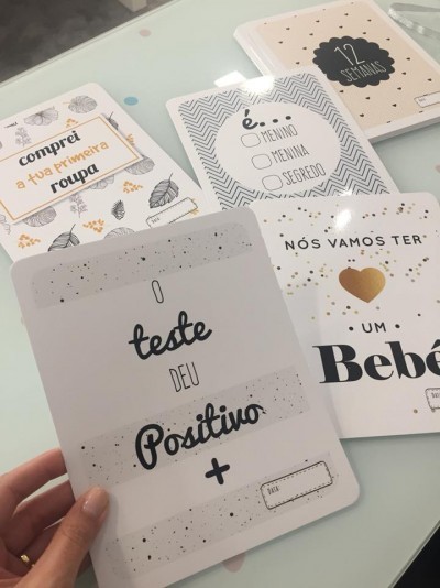 Cartões com mensagens de anúncio de gravidez em português, sobre superfície clara.
