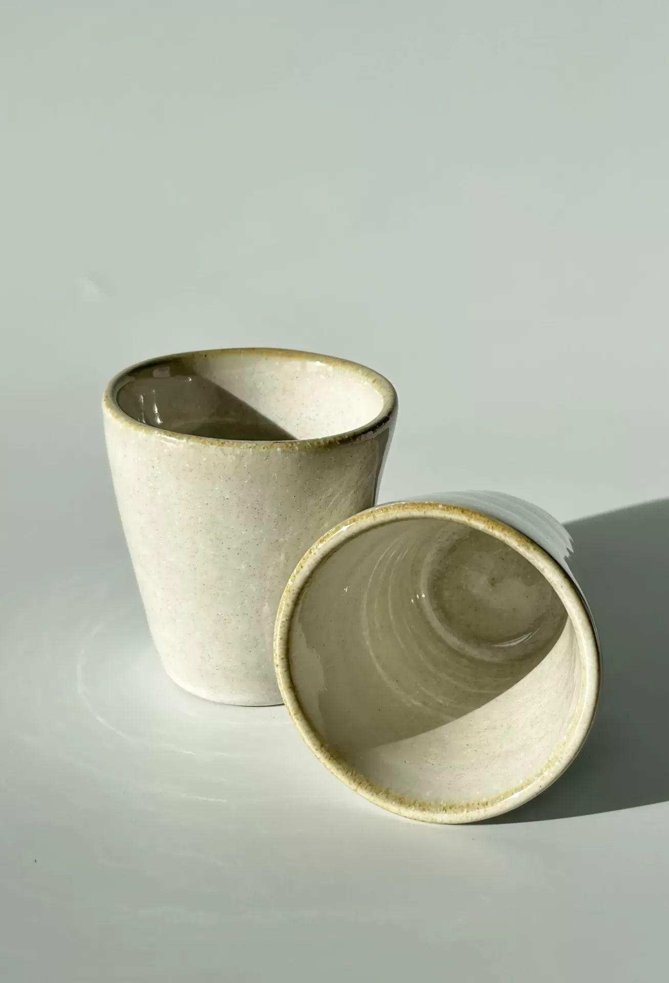 Duas chávenas de cerâmica bege claro com acabamento mate e bordas ligeiramente mais escuras