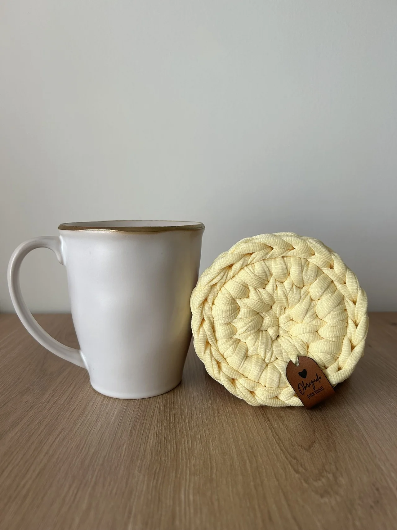 Caneca branca com bordo dourado e descanso de copos trançado amarelo com etiqueta de couro