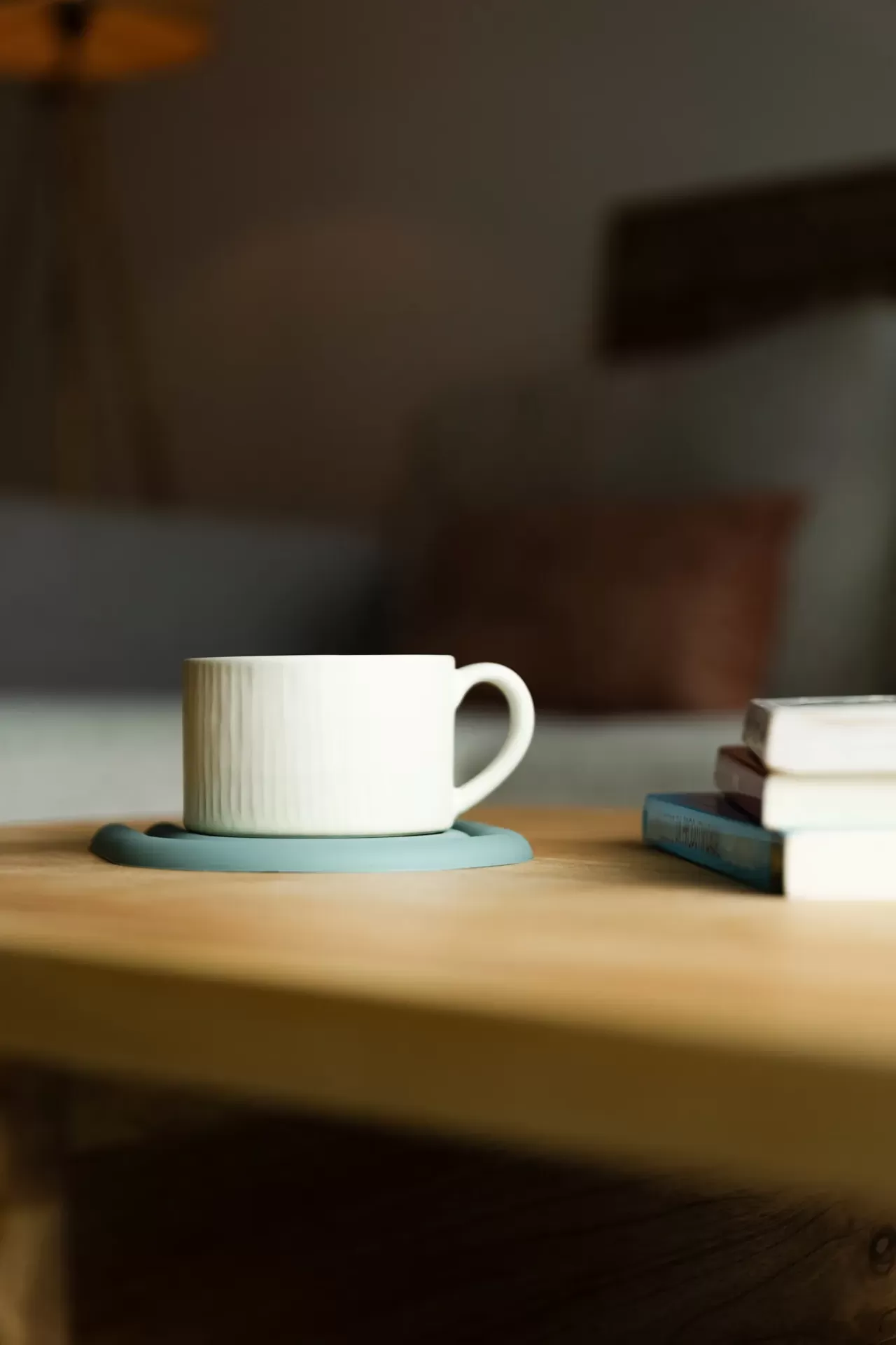 Chávena branca de cerâmica sobre suporte azul numa mesa de madeira com livros ao lado