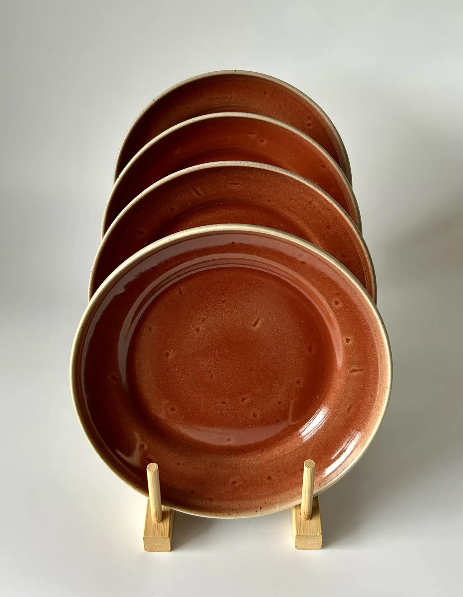 Conjunto de quatro pratos cerâmicos castanho-avermelhados com bordas bege em suporte de madeira