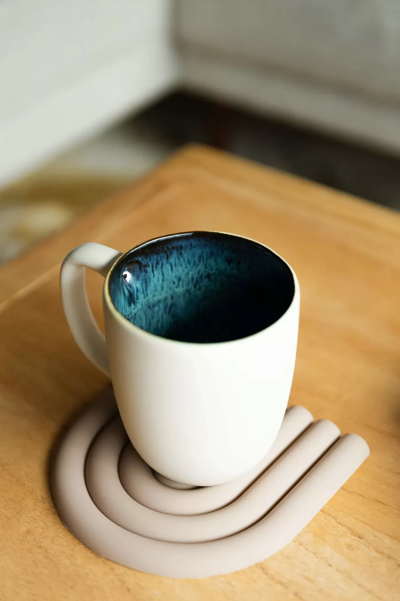 Caneca cerâmica branca com interior azul escuro e base de silicone bege sobre mesa de madeira clara
