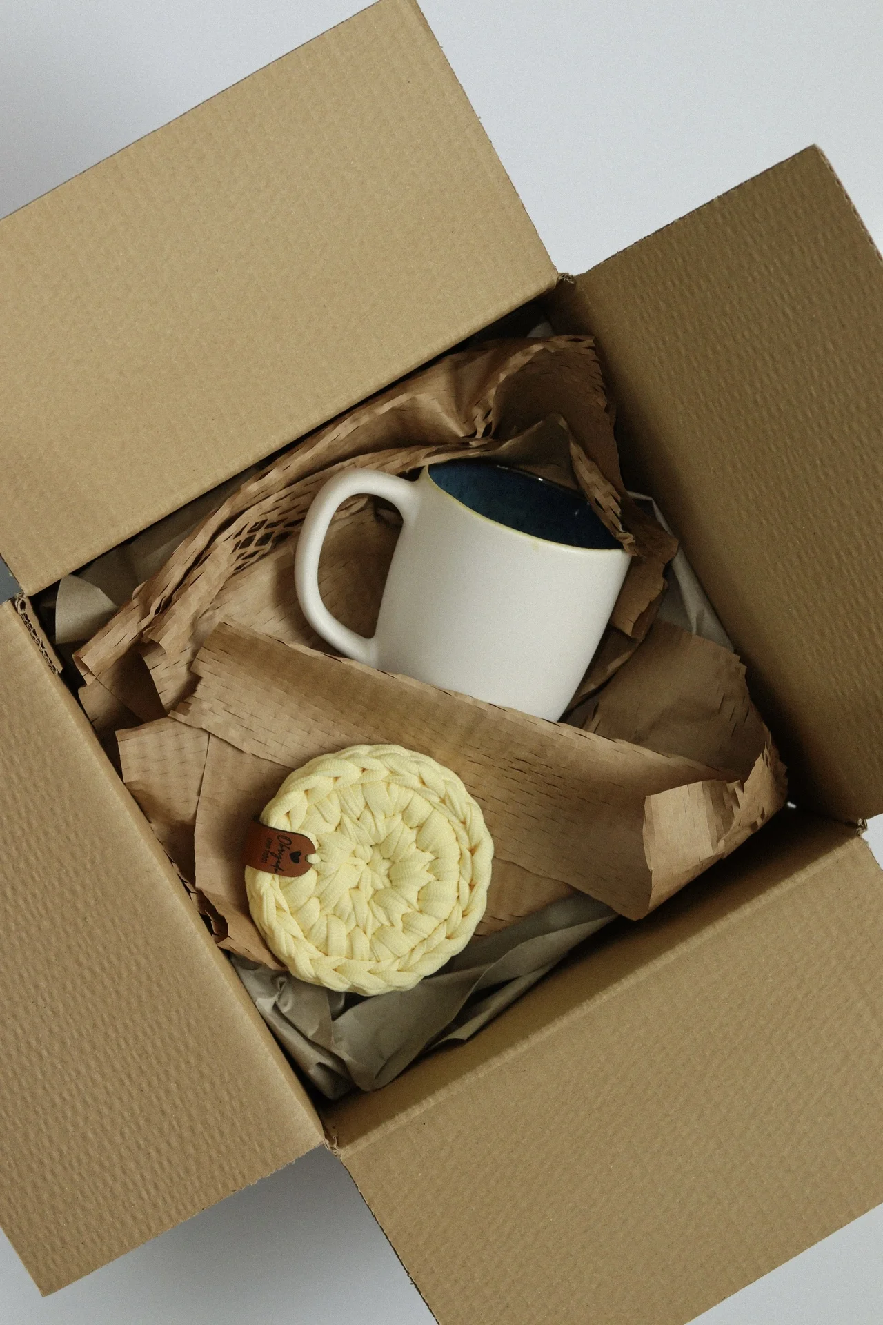 Caixa aberta com caneca branca com interior azul e objeto tricotado amarelo claro