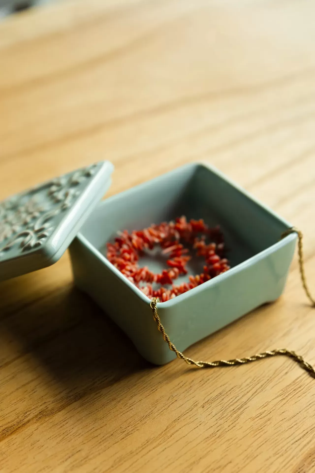 Caixa decorativa cinza com colar de pedras vermelhas e corrente dourada