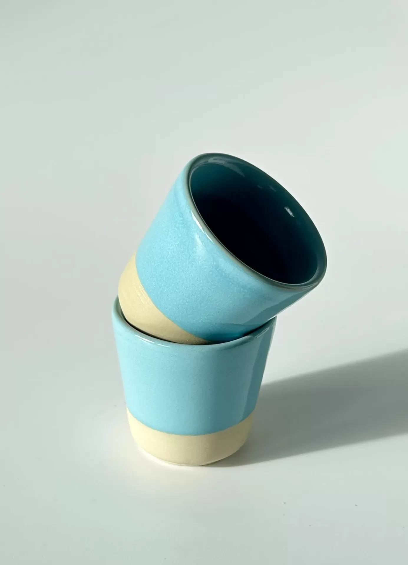 Dois copos de cerâmica azul turquesa empilhados sobre fundo branco
