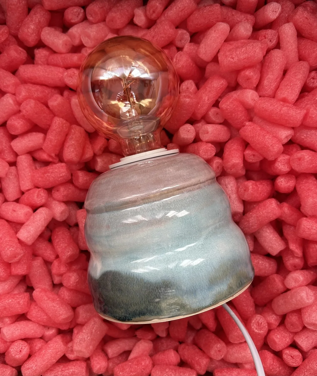 Lâmpada com bulbo âmbar e base cerâmica azul e cinza em enchimento rosa