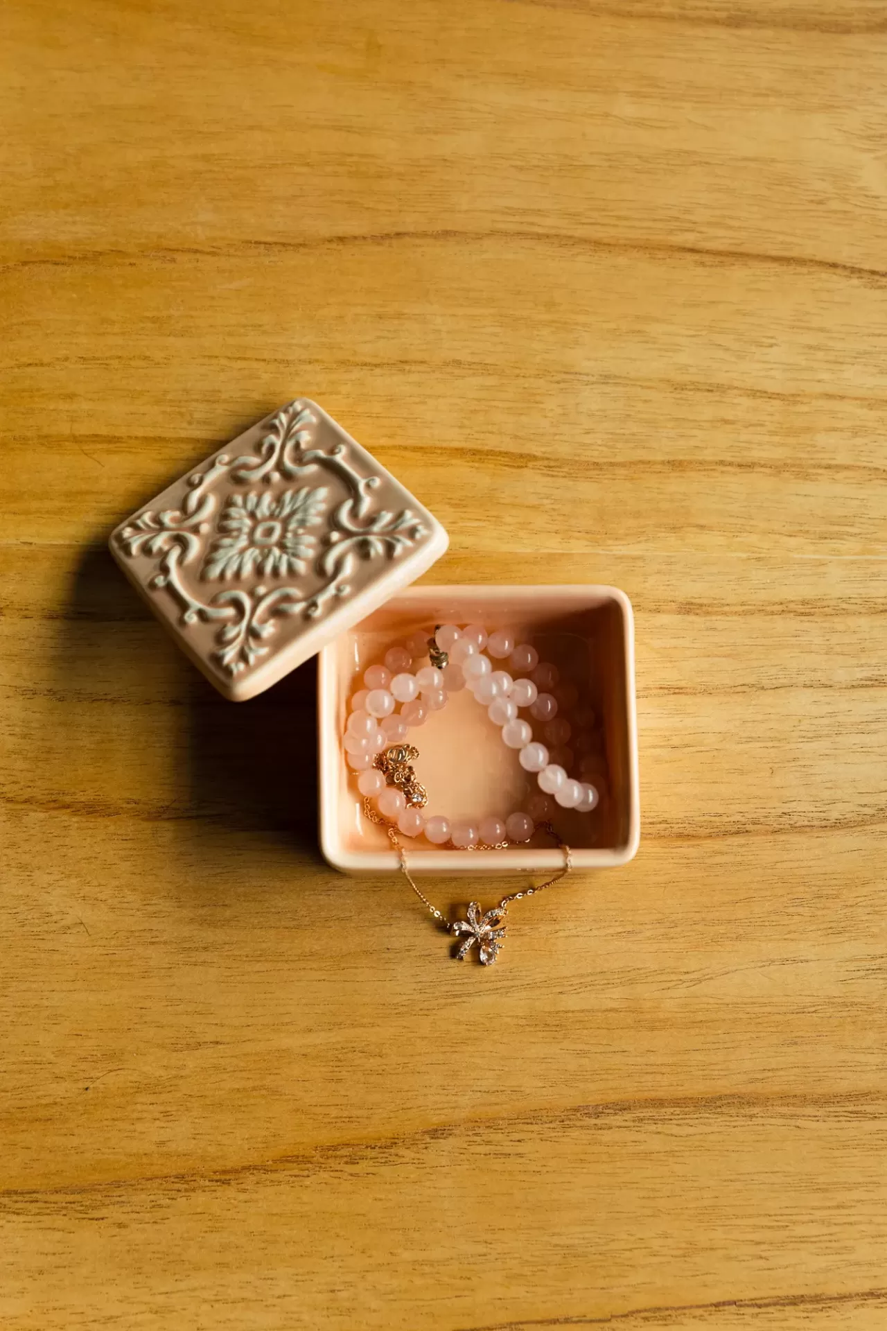 Caixa decorativa creme com pulseira rosada e corrente dourada com pendente floral
