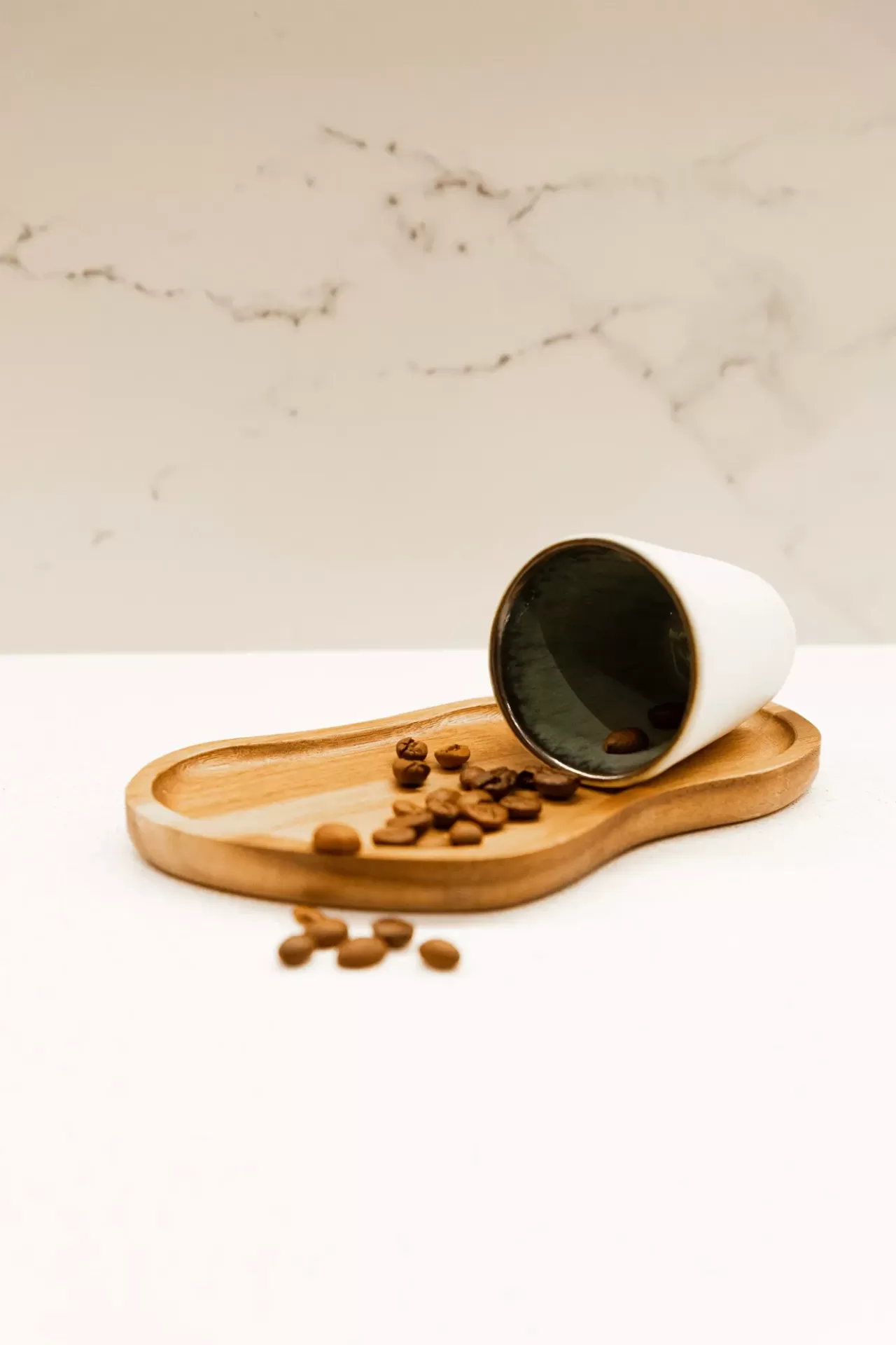 Cálice branco com interior preto deitado num tabuleiro de madeira com grãos de café