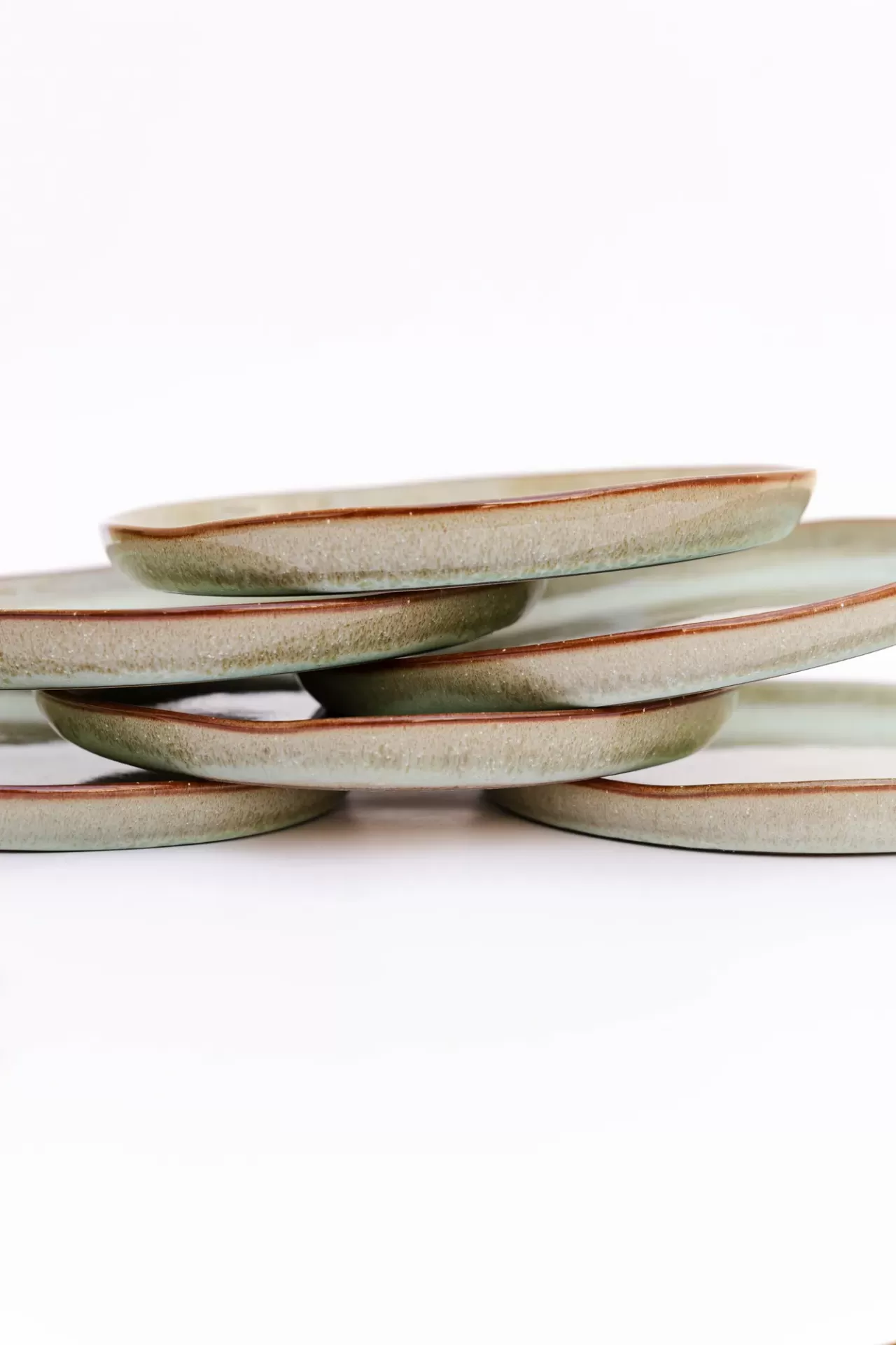 Conjunto de pratos redondos em cerâmica verde com borda castanha empilhados