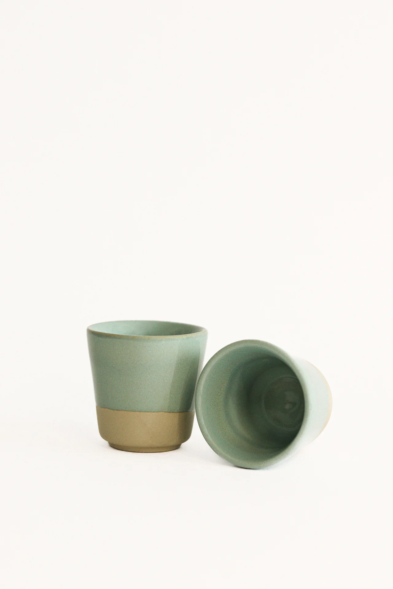 Dois copos cerâmicos verde claro com base castanha em fundo branco
