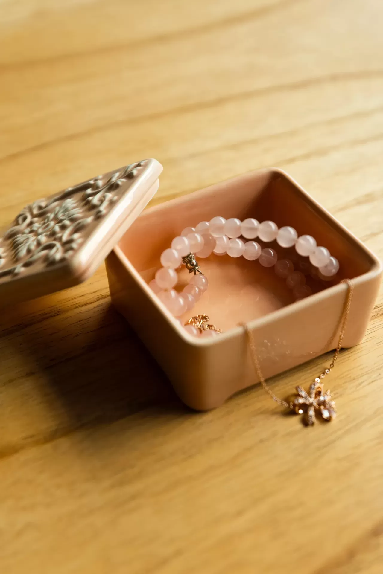 Caixa de cerâmica bege com jóias dentro e tampa lateral aberta sobre mesa de madeira