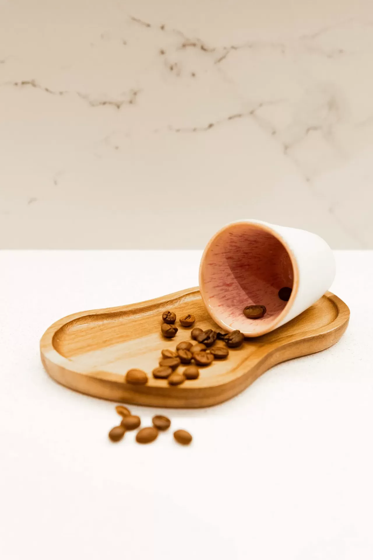 Xícara branca invertida com grãos de café sobre tabuleiro de madeira