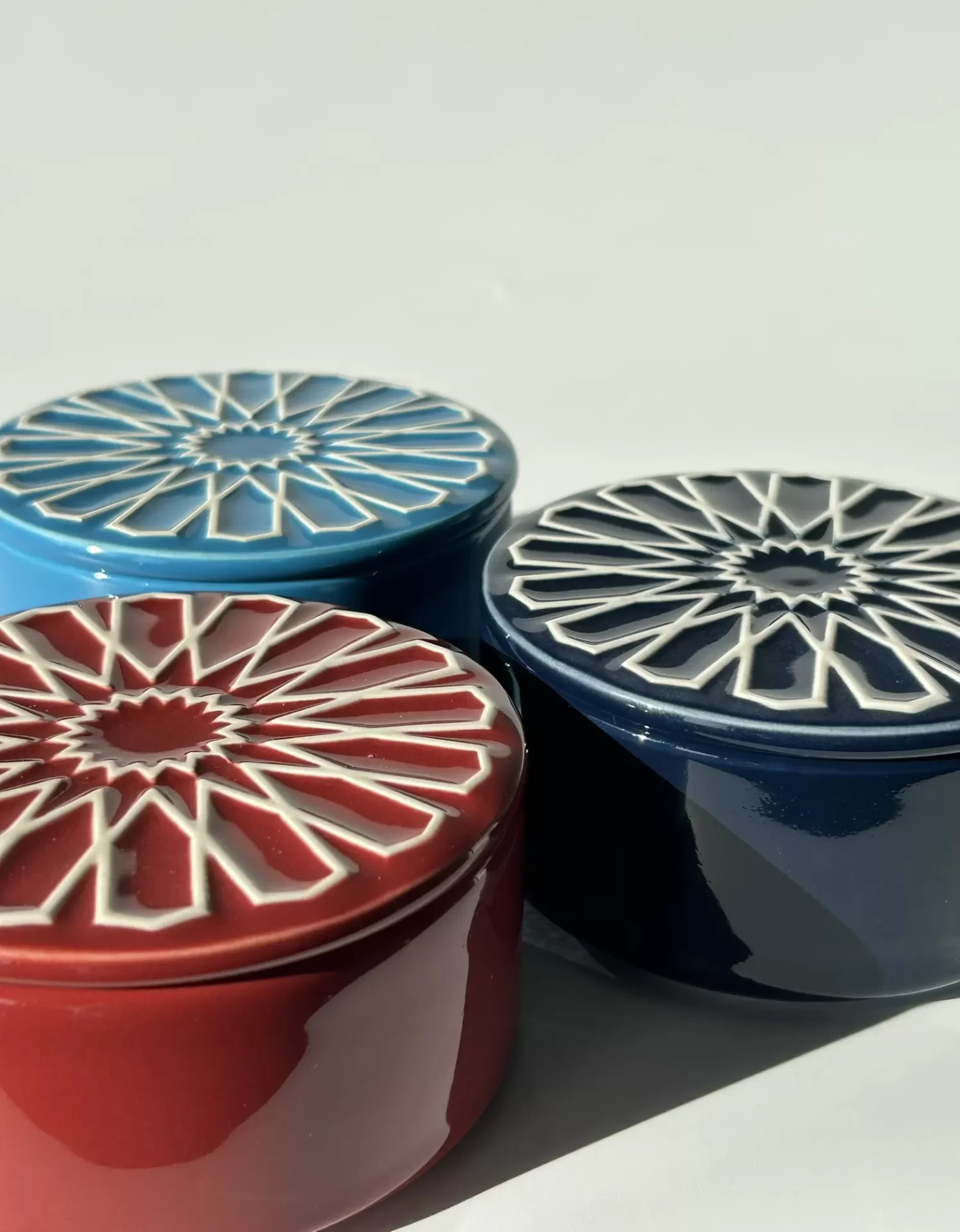 Três caixas redondas de cerâmica coloridas com tampas decoradas em padrão geométrico.