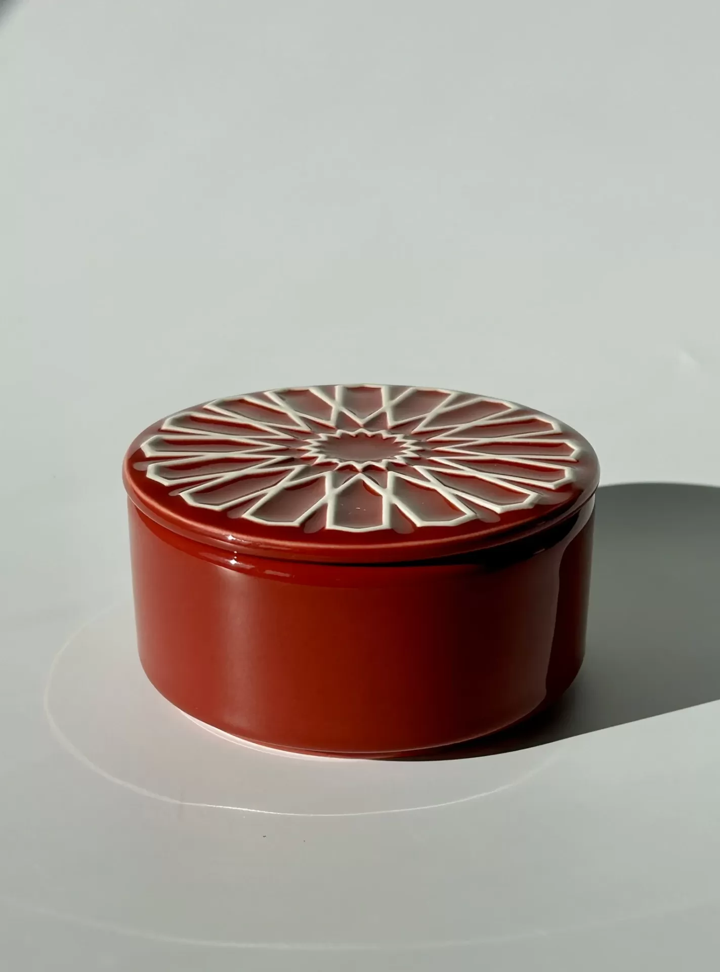 Caixa redonda vermelha com tampa decorada em padrão branco