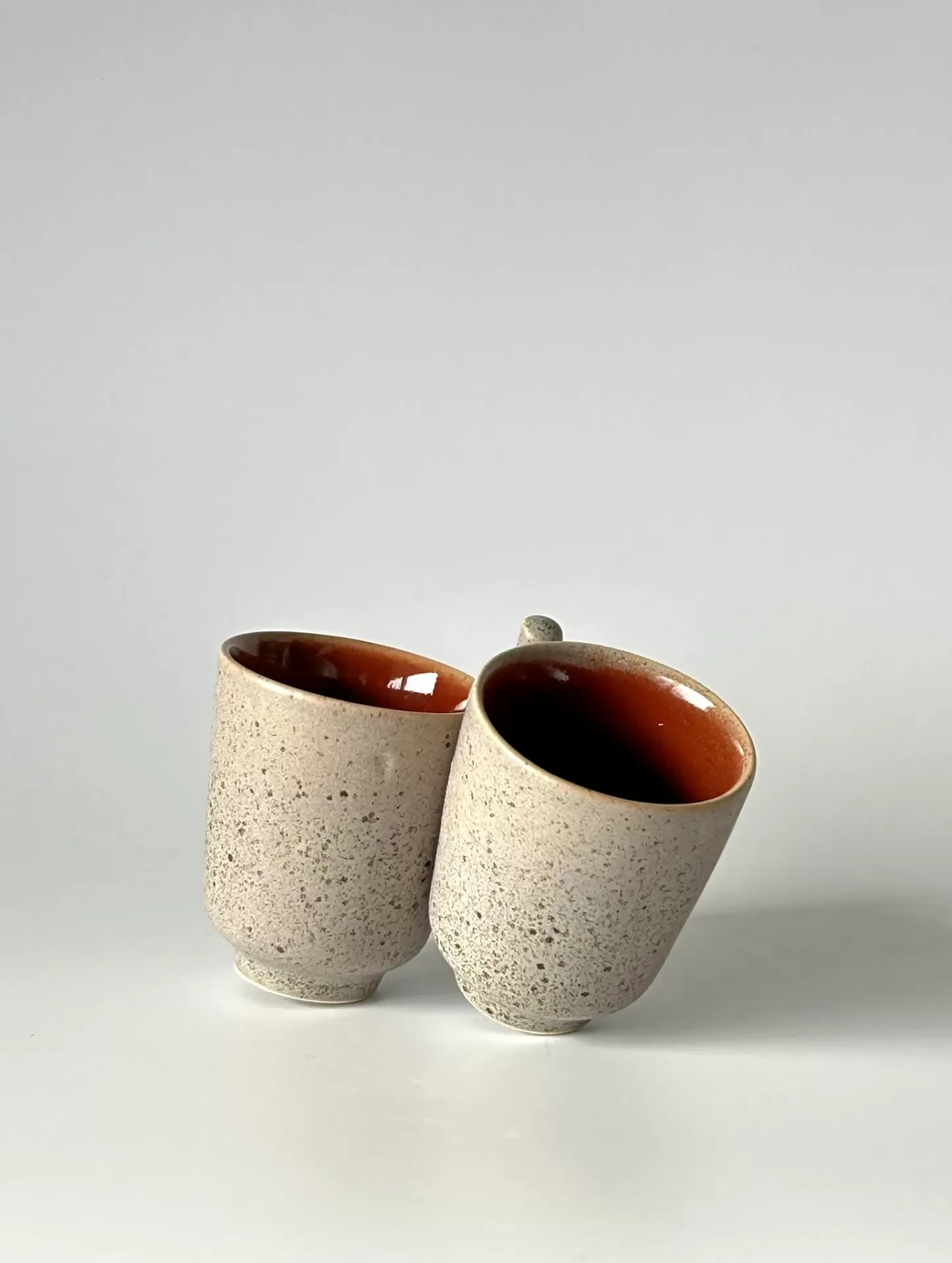 Dois copos de cerâmica cinza claro com interior laranja-avermelhado inclinados encostados.
