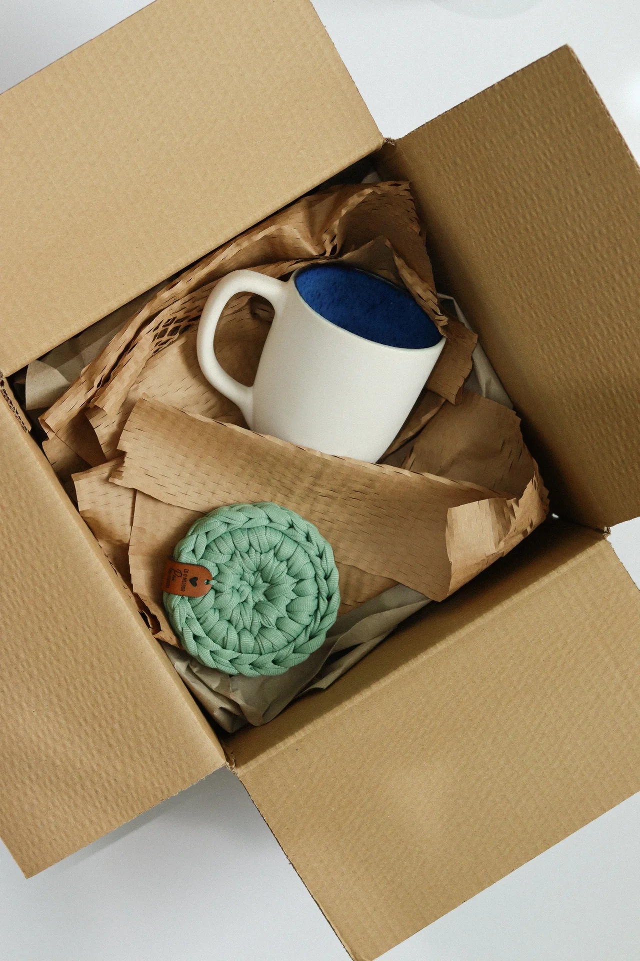 Caixa aberta com caneca branca azul e descanso de panela verde
