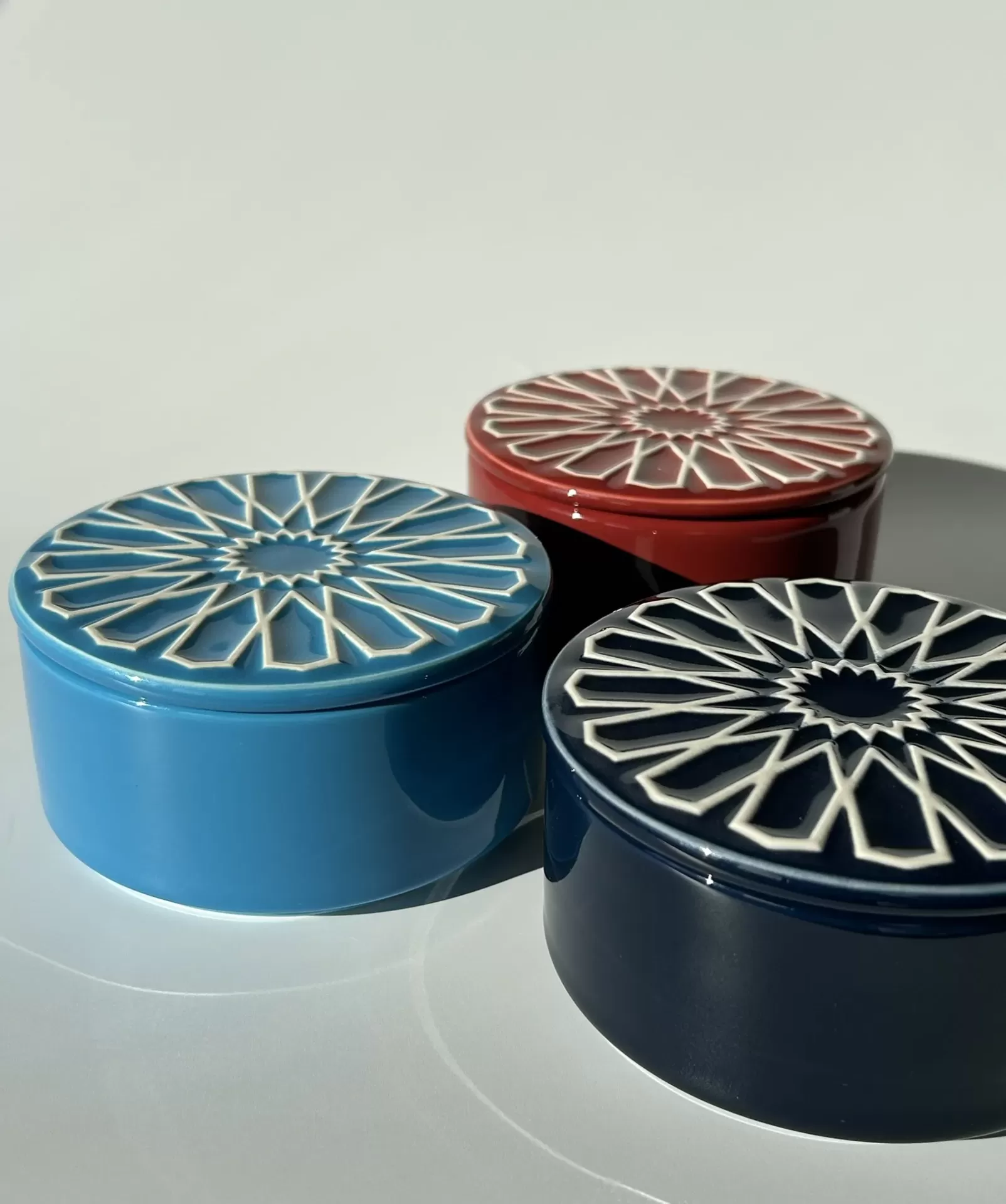 Três caixas redondas de cerâmica coloridas com padrão geométrico branco