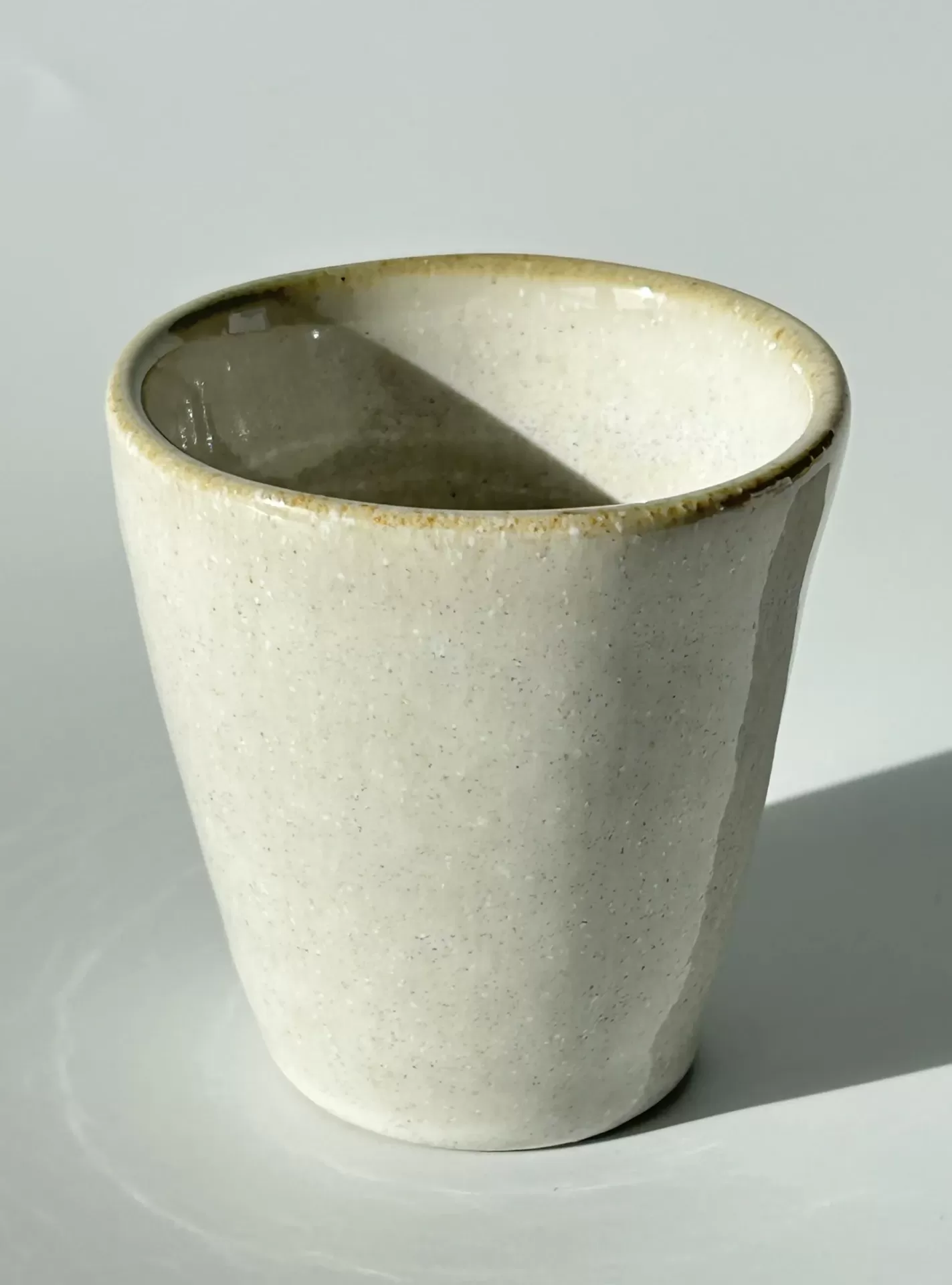 Copo de cerâmica bege claro com acabamento vidrado em fundo branco